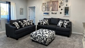 A living room with two sofas, a patterned ottoman, and a ceiling fan.