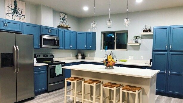 A modern kitchen with blue cabinets, stainless steel appliances, a central island with stools, and pendant lighting.
