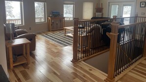 A spacious living room with hardwood flooring, large windows, a wooden staircase, and a cozy seating area. - Amazing  Views--Spacious 3BR, outdoor barrel sauna, dog friendly (Hartsel)