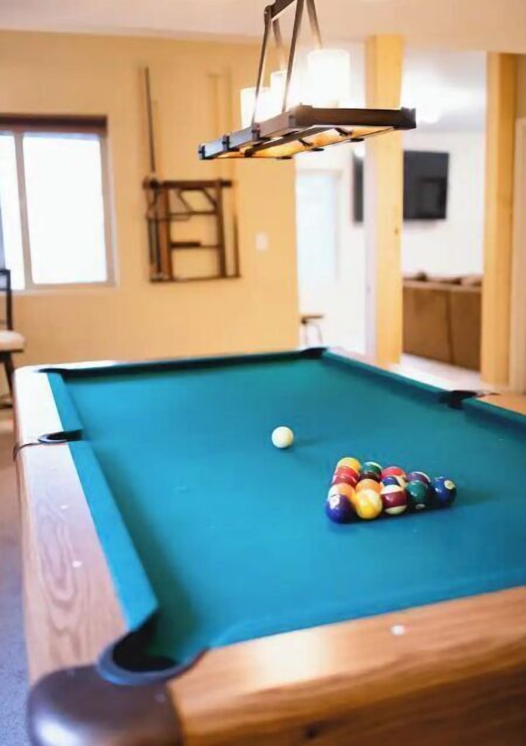 A pool table with balls, a hanging light fixture, and a wooden chair.