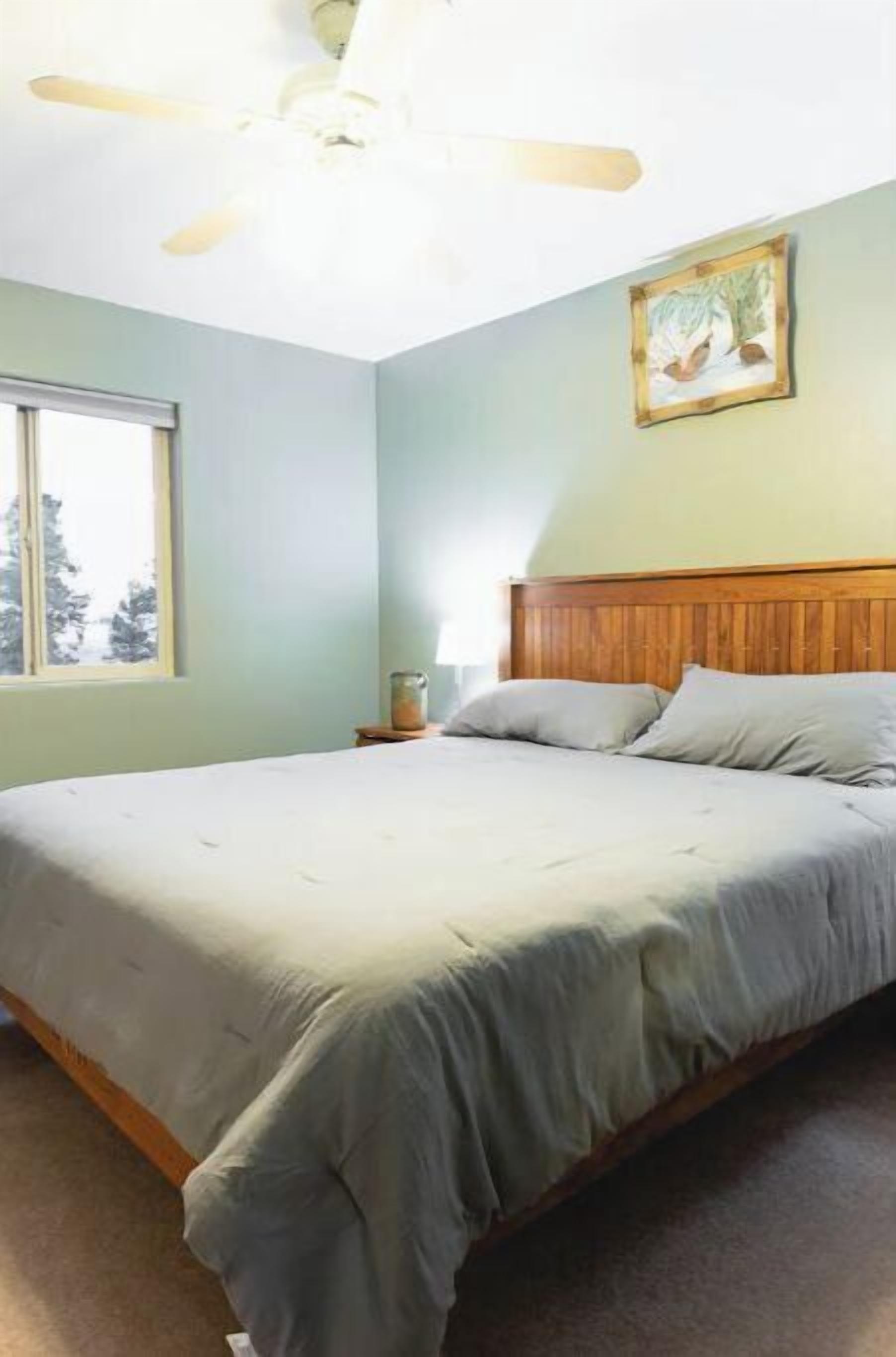 Un dormitorio con una cama, ventilador de techo, ventana y un cuadro en la pared.