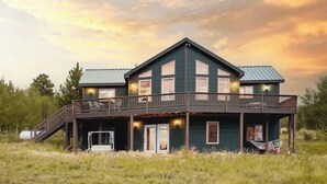A two-story building with a balcony and a covered area, surrounded by grass and trees. - Amazing  Views--Spacious 3BR, outdoor barrel sauna, dog friendly (Hartsel)