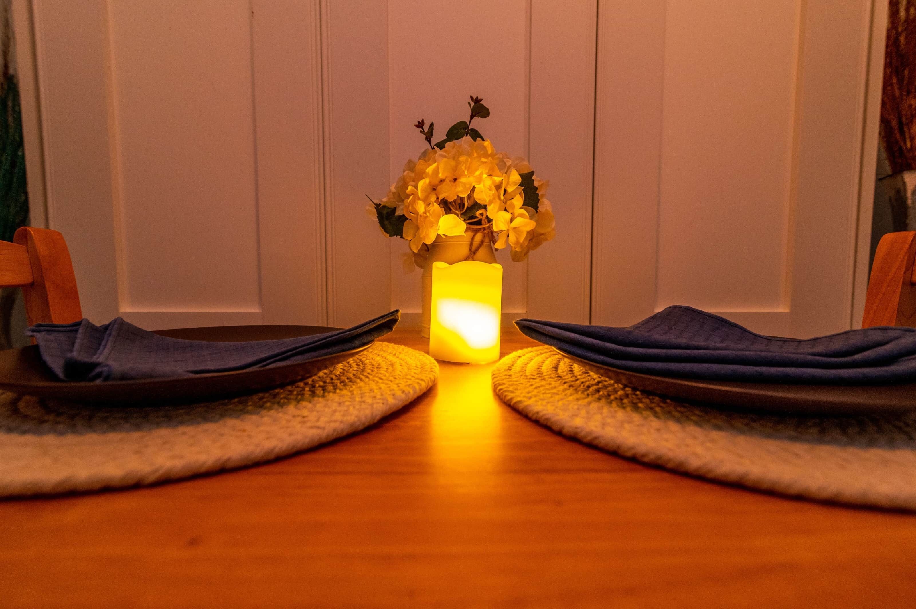 A dining table with a candle and a vase of flowers in the center.