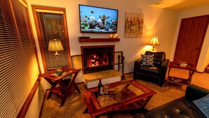 Ein gemütliches Wohnzimmer mit Kamin, Fernseher und bequemen Sitzgelegenheiten.