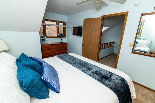 Une chambre à coucher comprenant un lit, une commode, un téléviseur et une porte donnant sur un escalier.