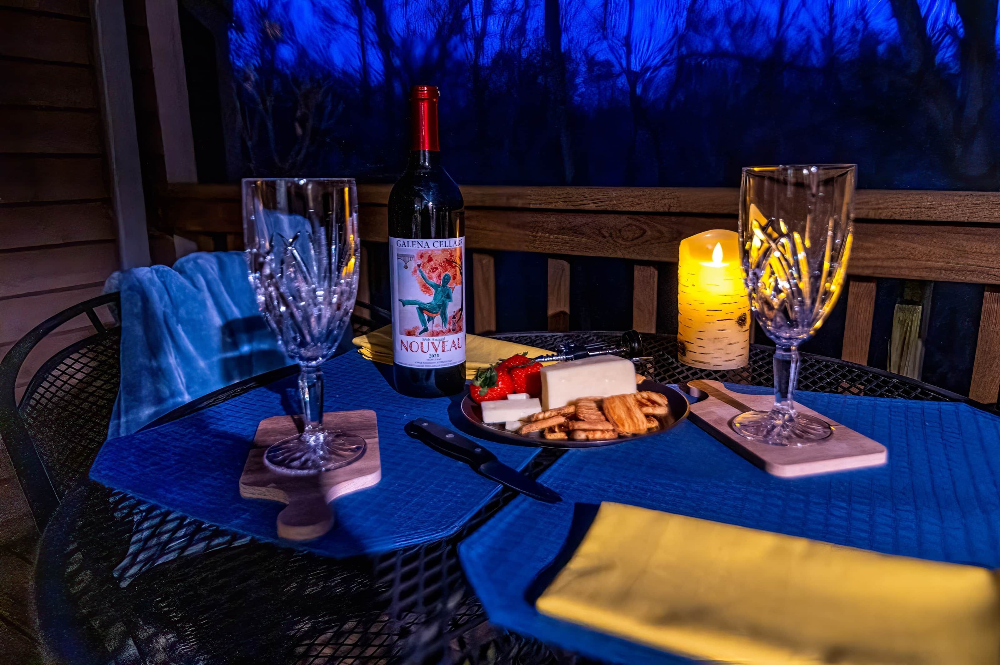 A table set with a bottle of wine, glasses, a candle, and a plate of cheese and crackers.