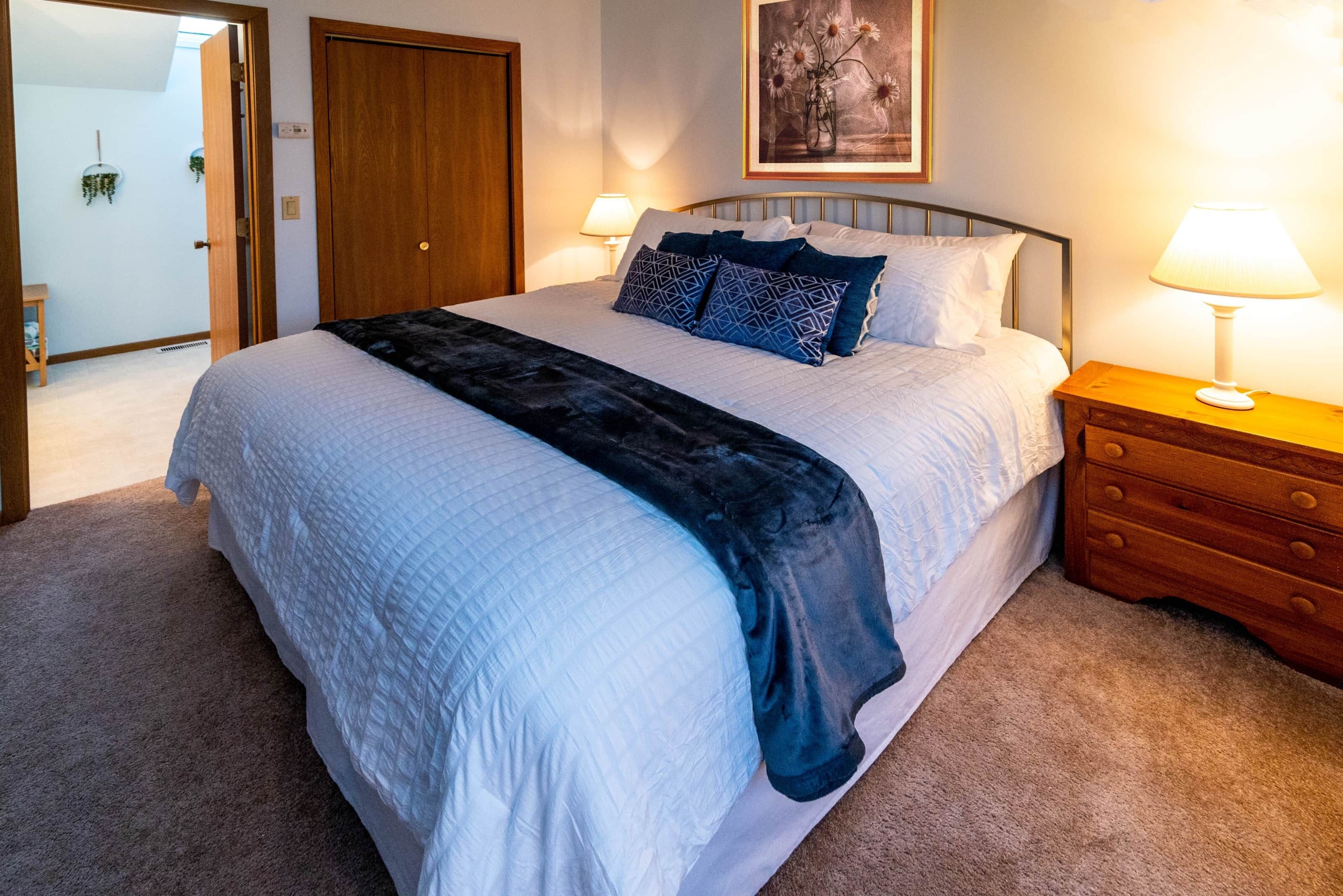 A neatly made bed with a quilted cover, two bedside lamps, and a wooden nightstand.