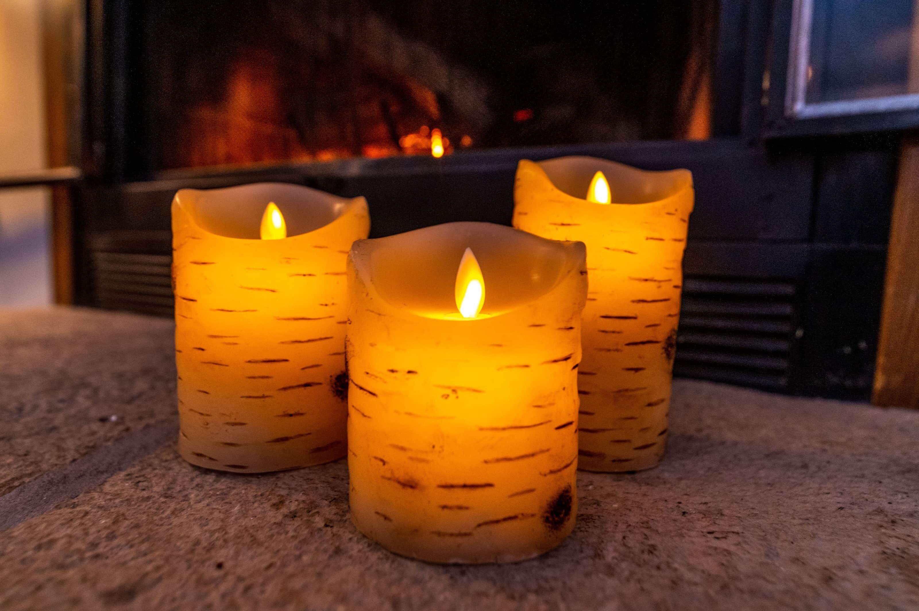 Three candles on a carpeted floor with a fireplace in the background.