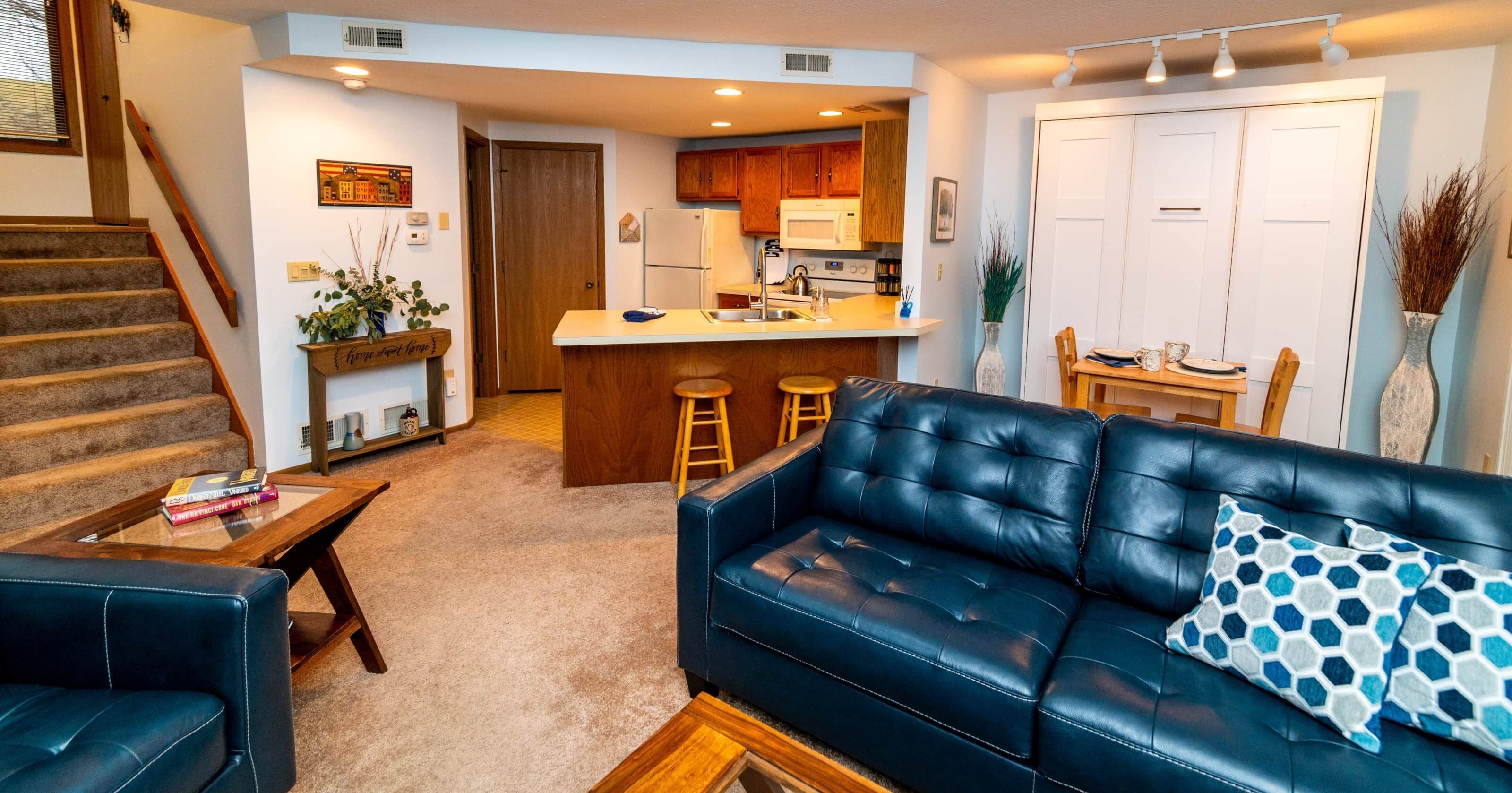 A modern living room with a blue leather sofa, a coffee table, and a staircase.