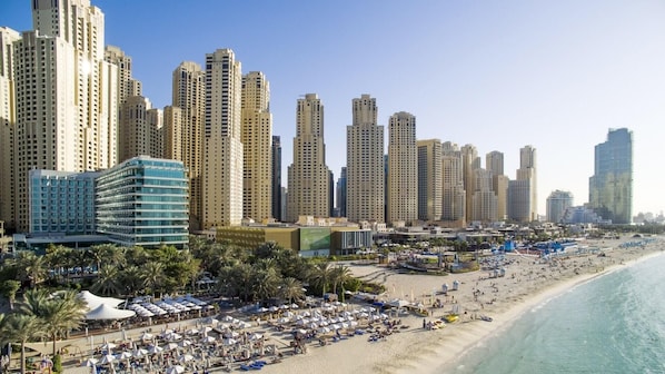 Eine Küstenstadt mit Hochhäusern, einem Strand mit Sonnenschirmen und Liegestühlen sowie einem klaren, blauen Meer.