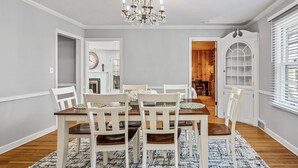 A dining room with a chandelier, white chairs, a wooden table, and a patterned rug. - 1419-Walk to Mayo St Mary-Ritabnb Cheerful 5br+6baths,1 min walk to St.Marys (Rochester)