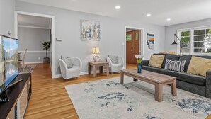 A living room with a wooden floor, a grey sofa, two white armchairs, a coffee table, and a TV. - 1419-Walk to Mayo St Mary-Ritabnb Cheerful 5br+6baths,1 min walk to St.Marys (Rochester)