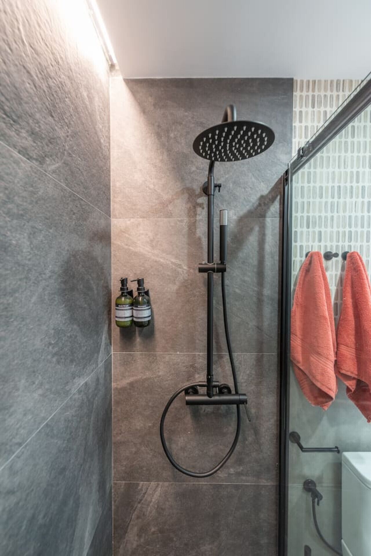 A modern shower with a handheld head, a glass enclosure, and a towel rack with two towels.
