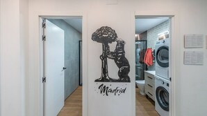 Un pasillo con una puerta que da a un área de lavandería, un mural en blanco y negro, y un letrero que dice "Madrid".