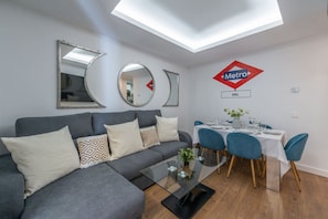 Un salon moderne avec un canapé gris, une table à manger dressée pour quatre personnes et un panneau de signalisation du métro accroché au mur.