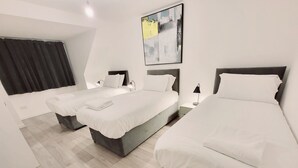 Ein Hotelzimmer mit drei Betten, einem großen abstrakten Gemälde und einem Fenster mit dunklen Vorhängen.