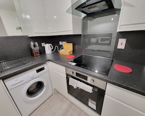 A modern kitchen with a built-in oven, a microwave, a kettle, and a washing machine.