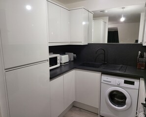 A compact kitchen with white cabinets, a microwave, a toaster, a sink, and a washing machine.