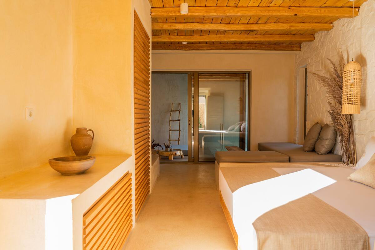 A room with a wooden ceiling, a bed, a sofa, and a small table with a bowl and vase.