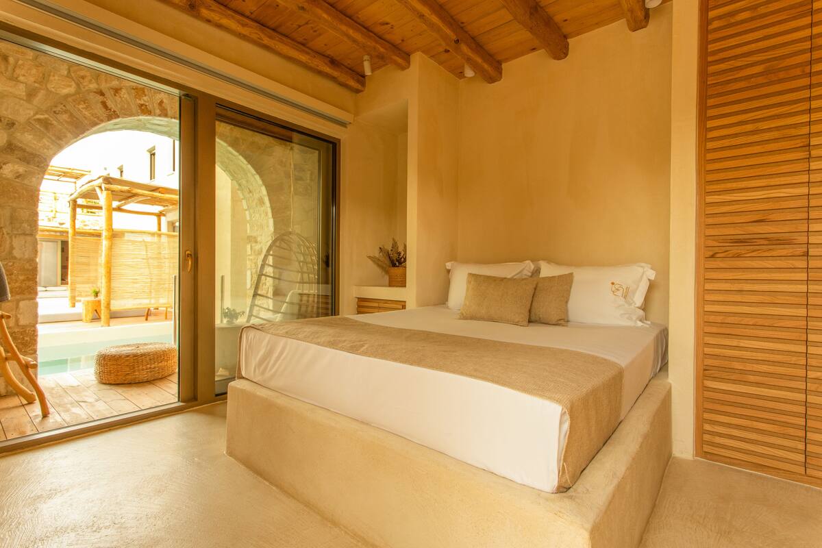 A bedroom with a large bed, a wooden ceiling, a stone archway, and a view of an outdoor area.