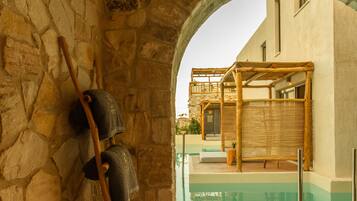 A stone-walled room with a wooden floor, a wicker ottoman, and a view of an outdoor pool area.