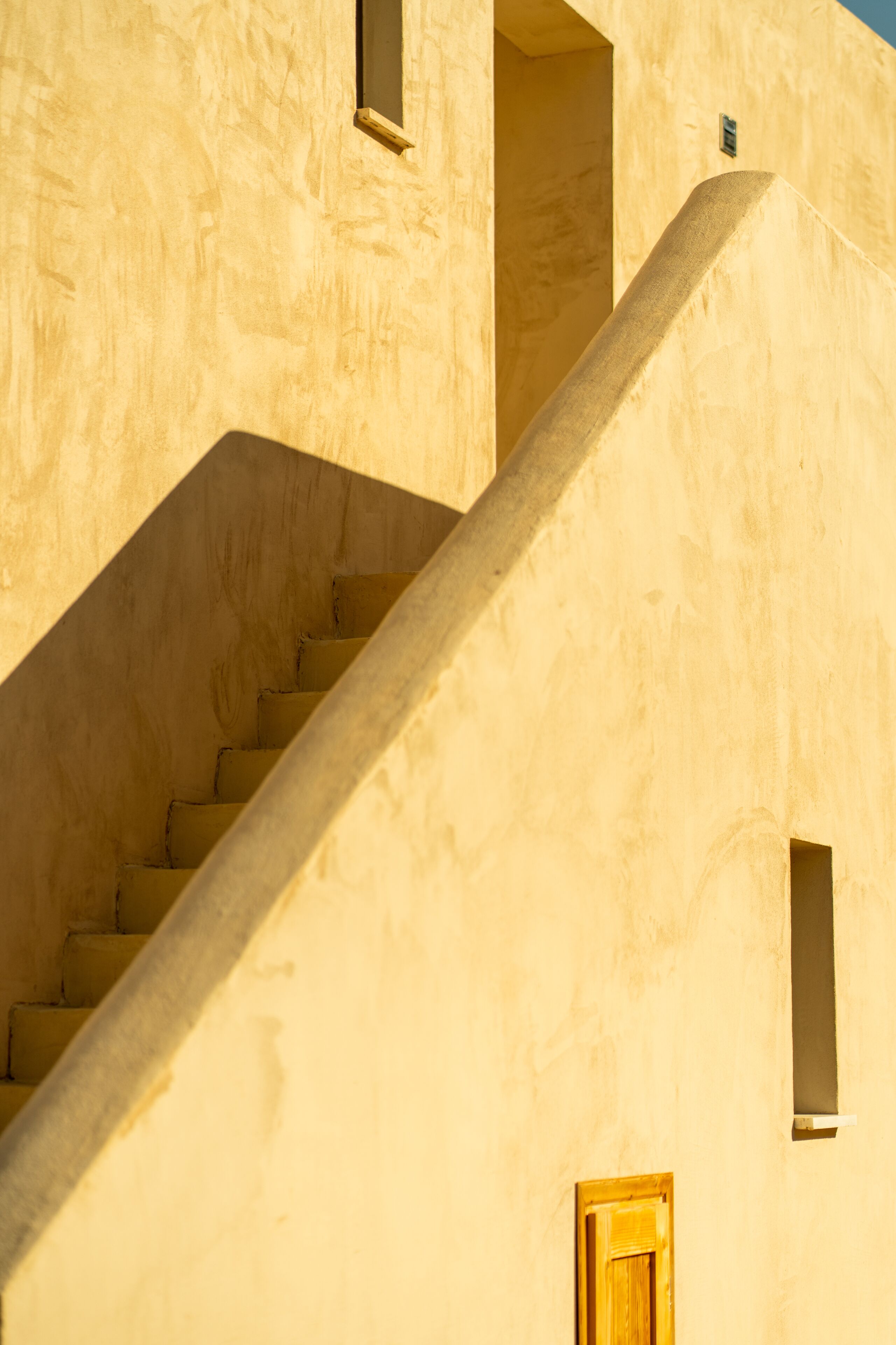 Una escalera conduce a un nivel superior de un edificio con fachada sencilla y una ventana pequeña.