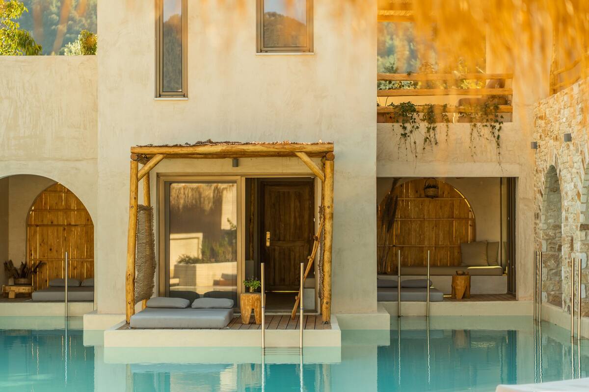 A pool area with a wooden pergola, seating, and a stone wall.