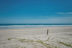 Una spiaggia con un palo di legno in primo piano e un cielo azzurro limpido.