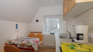 Une petite cuisine équipée d’une table à manger, de chaises, d’une machine à café et d’une fenêtre avec des stores.