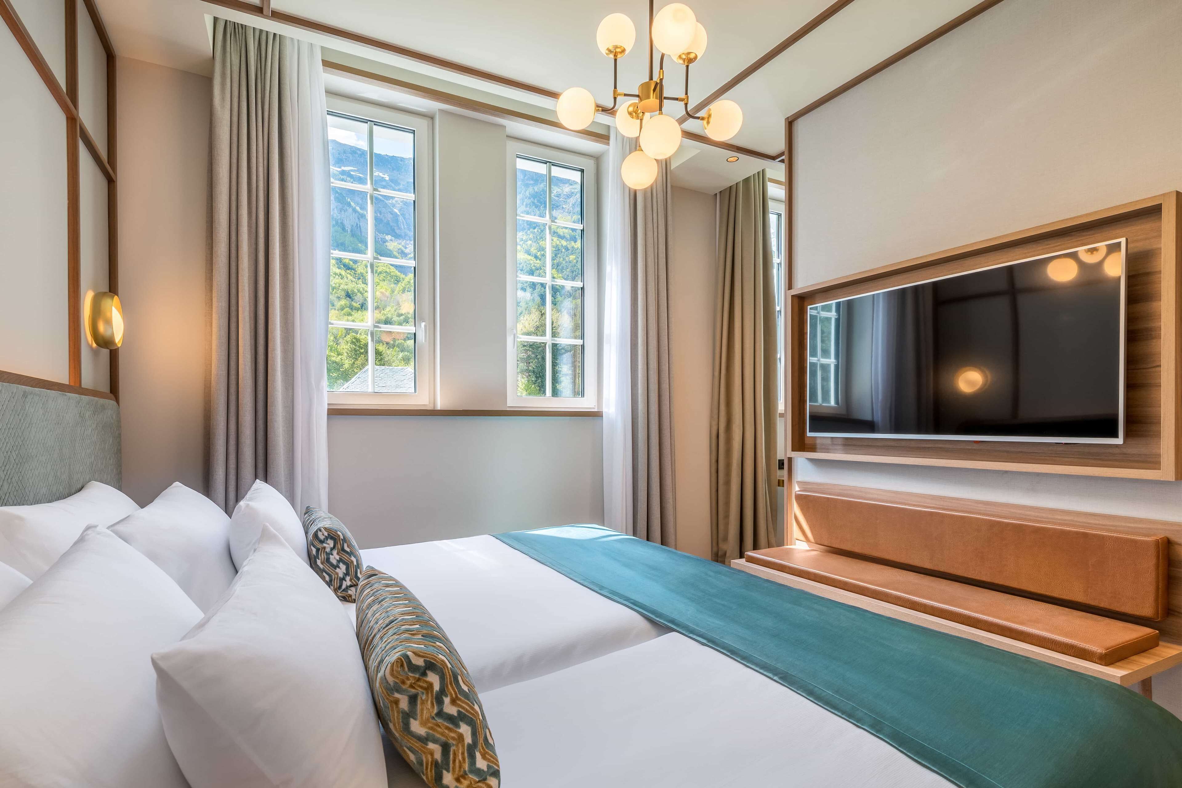 Une chambre d’hôtel avec un grand lit, un téléviseur fixé au mur et une fenêtre avec des rideaux.