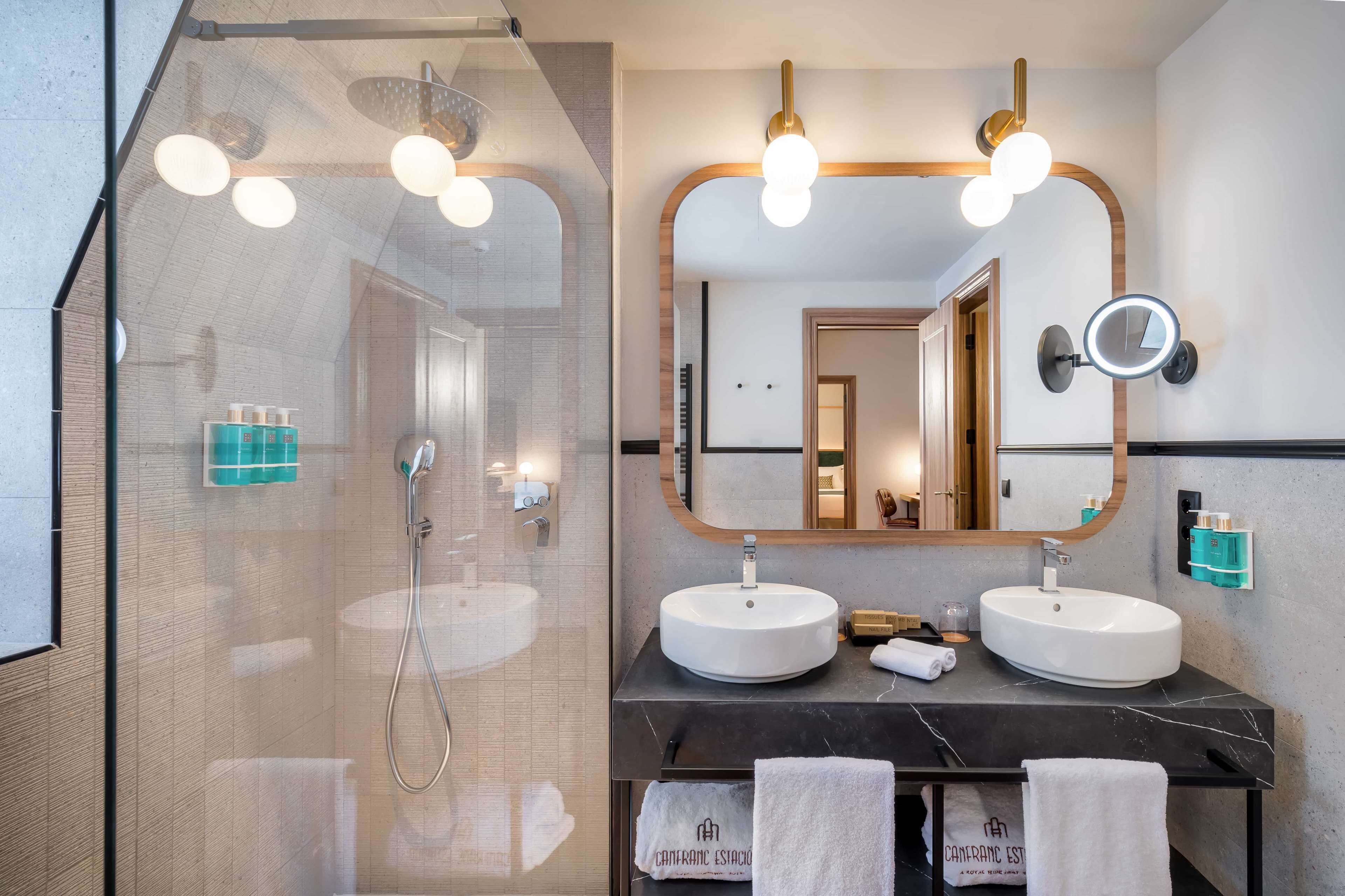 Een moderne badkamer met twee wastafels, een grote spiegel en een douche met glazen wanden.