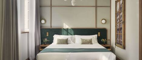 Una habitación de hotel con una cama grande, mesitas de noche, un banco, un candelabro y una ventana con cortinas.