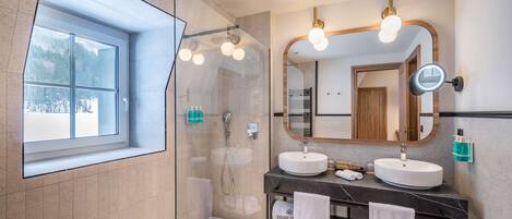 A modern bathroom with two sinks, a large mirror, and a shower.
