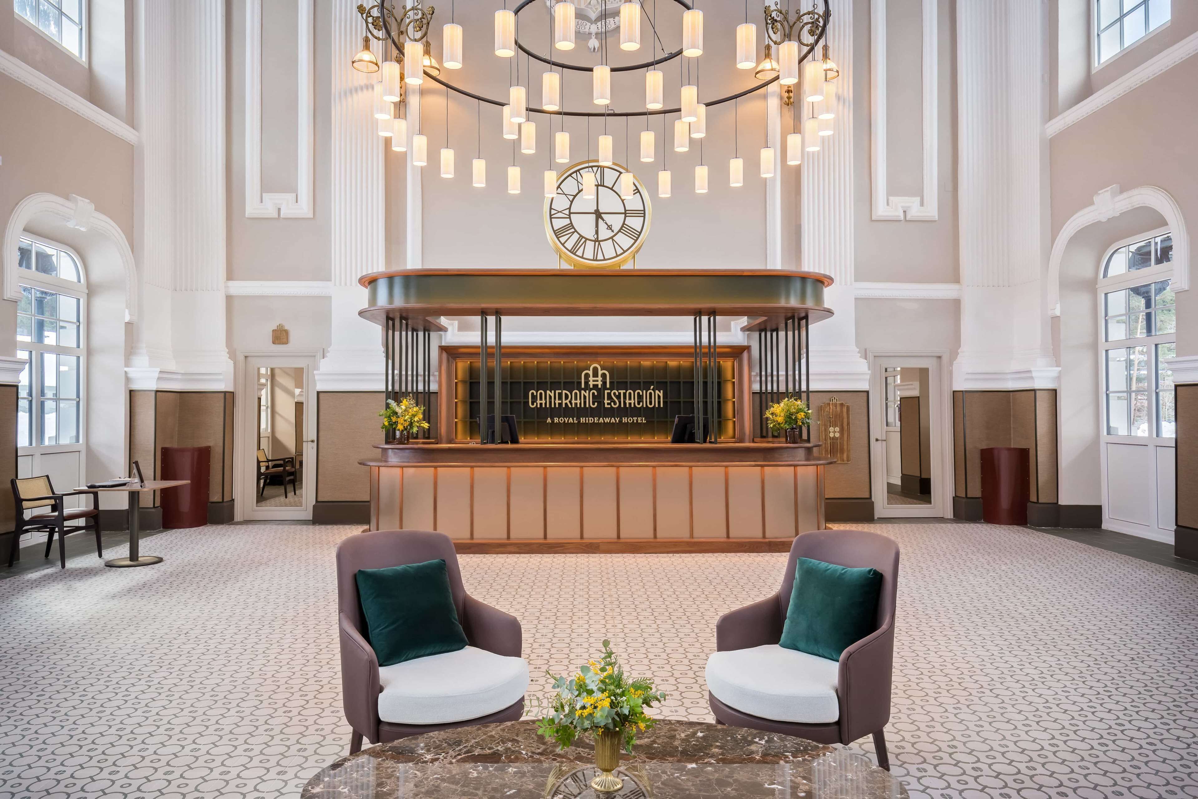 A spacious lobby with a reception desk, two armchairs, a coffee table, and a large chandelier.
