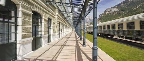 Un quai de gare couvert, doté d’une longue passerelle droite, de colonnes et d’un train sur les voies.