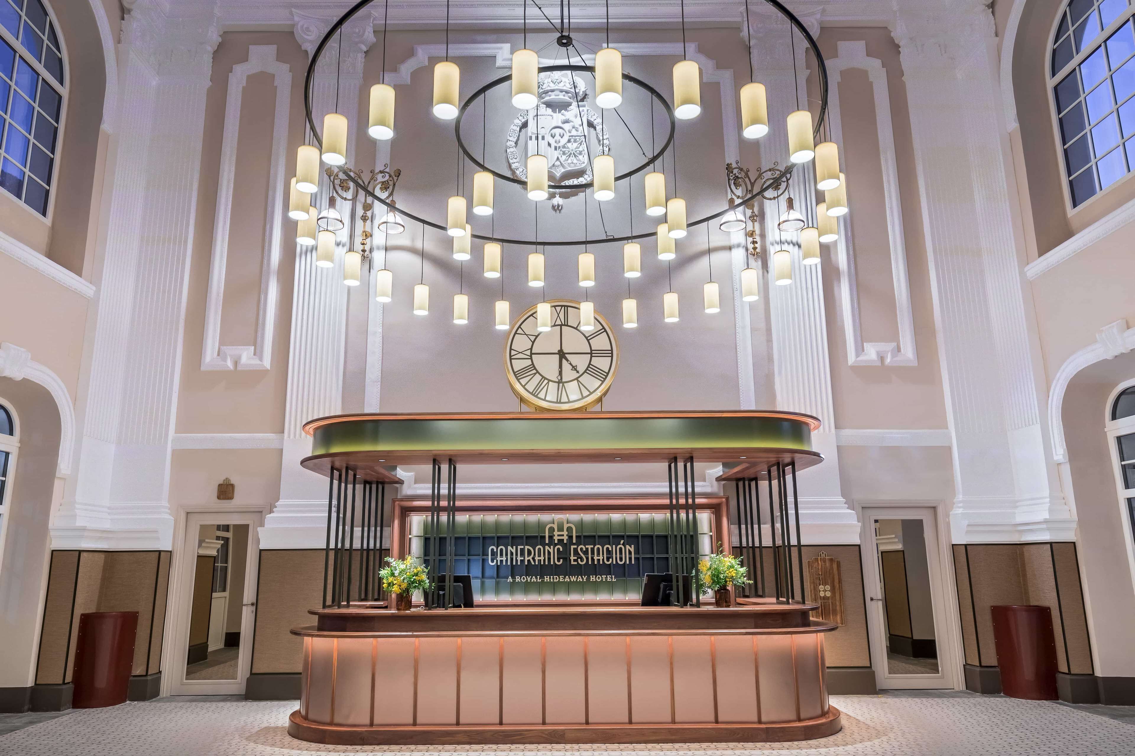 Een receptie met een klok, een ronde kroonluchter, en een bord met de tekst 'CANFRANC ESTACION A ROYAL HIDEAWAY HOTEL'.