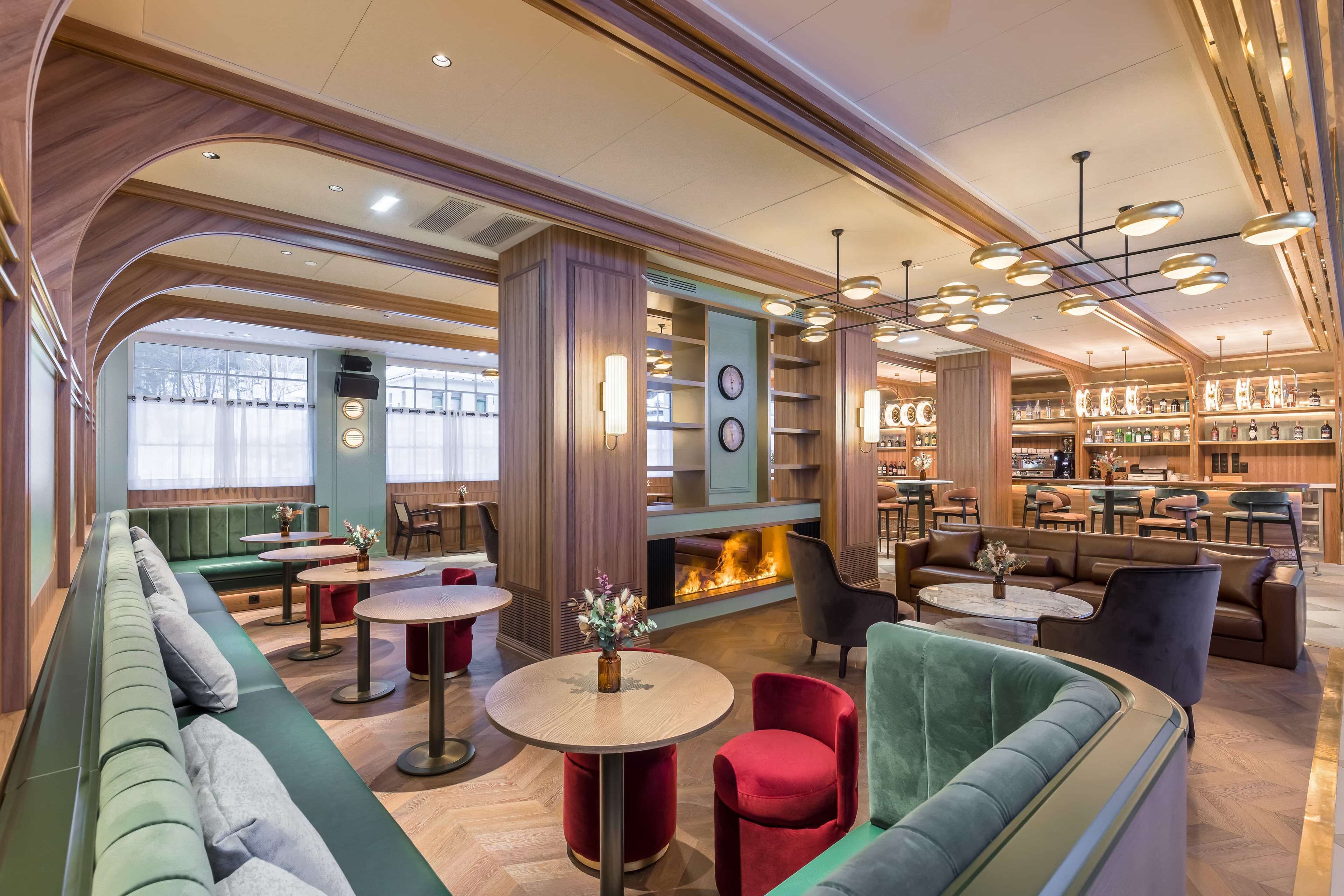 A modern lounge area with seating, tables, a fireplace, and a bar area.