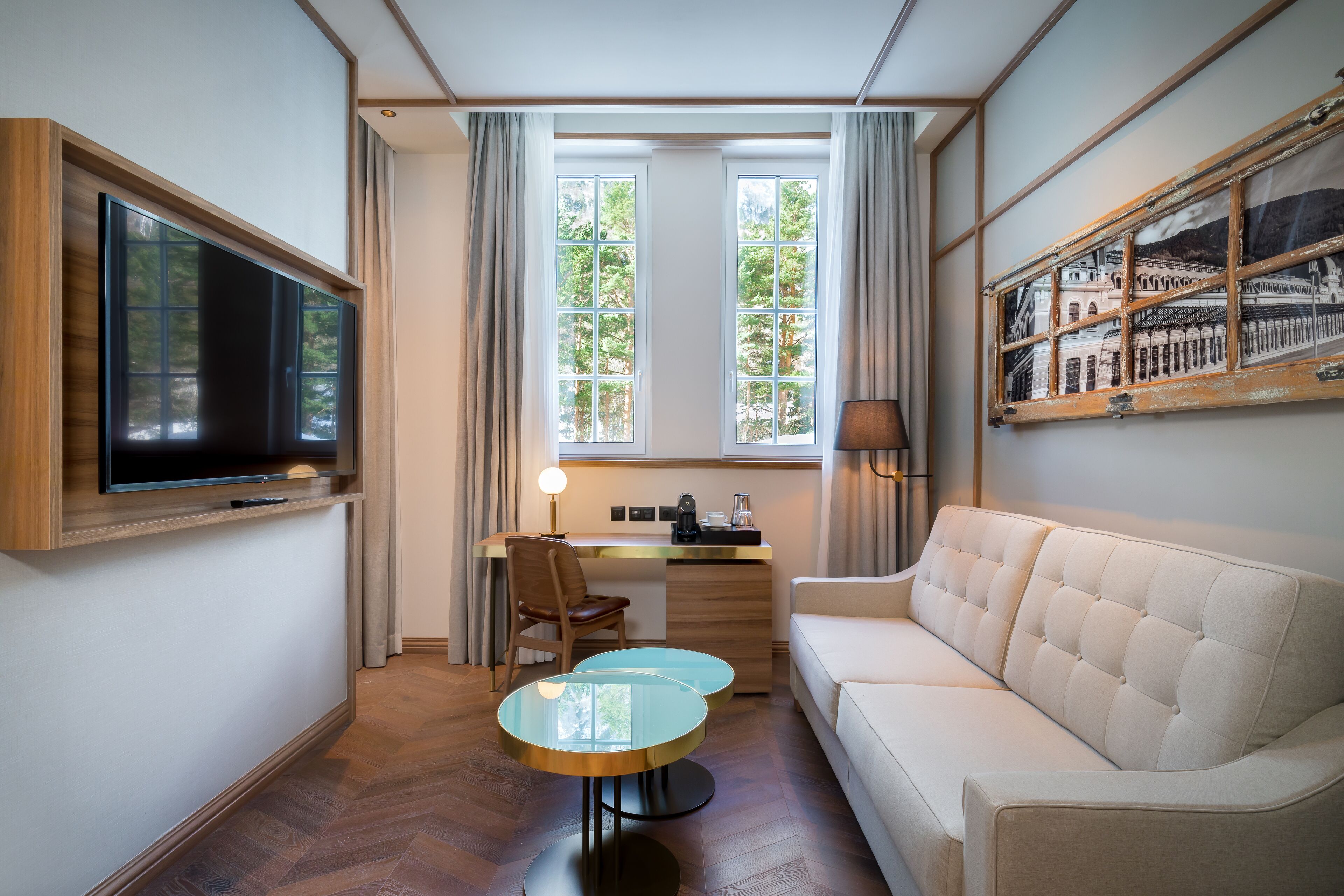 A modern hotel room with a flat-screen TV, a sofa, a dining table, and a desk with a lamp.