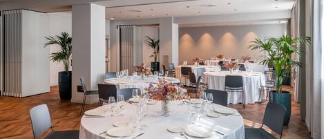 A spacious dining area with round tables set for a formal event, featuring white tablecloths and floral centerpieces.