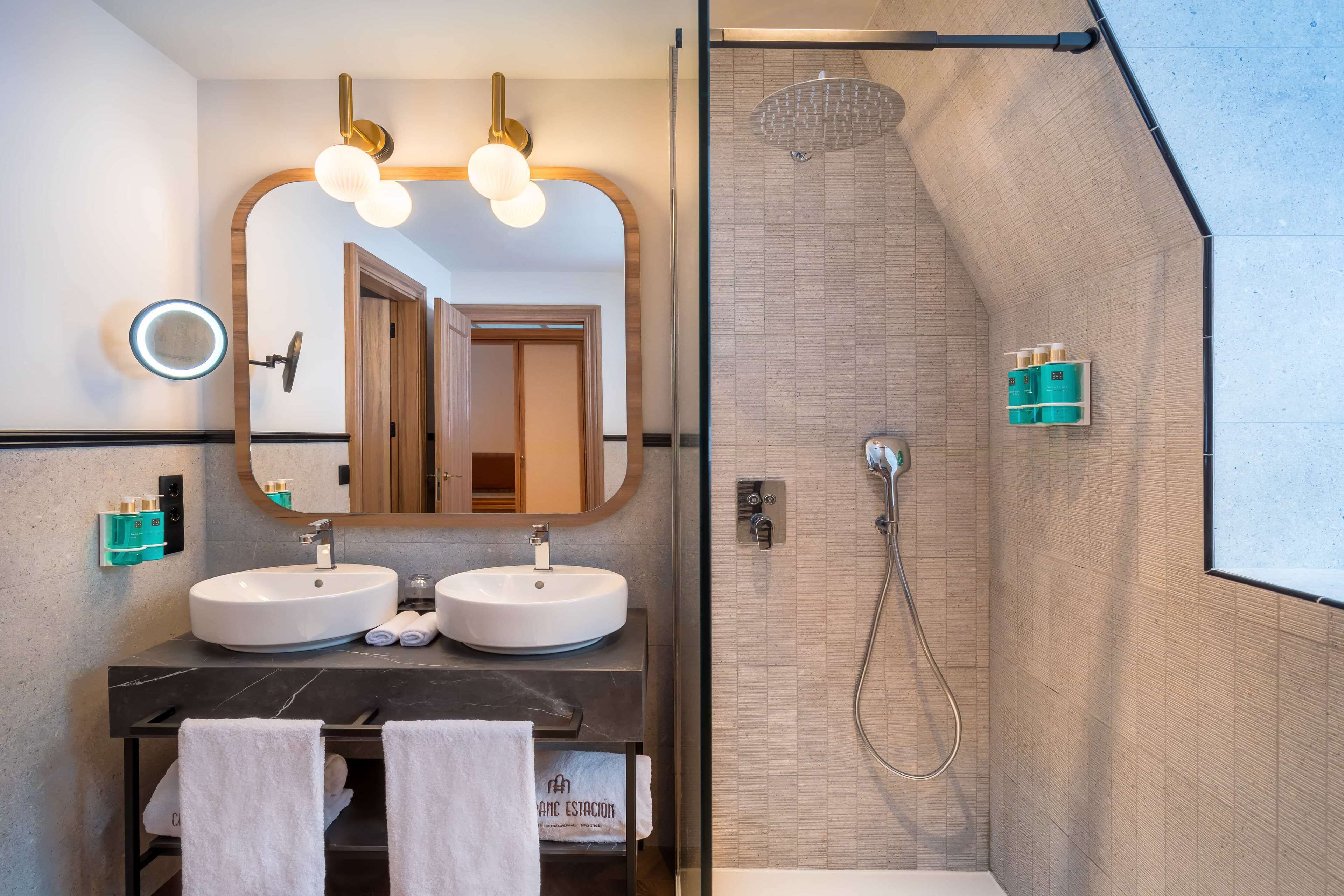 A modern bathroom with two sinks, a large mirror, and a shower area.