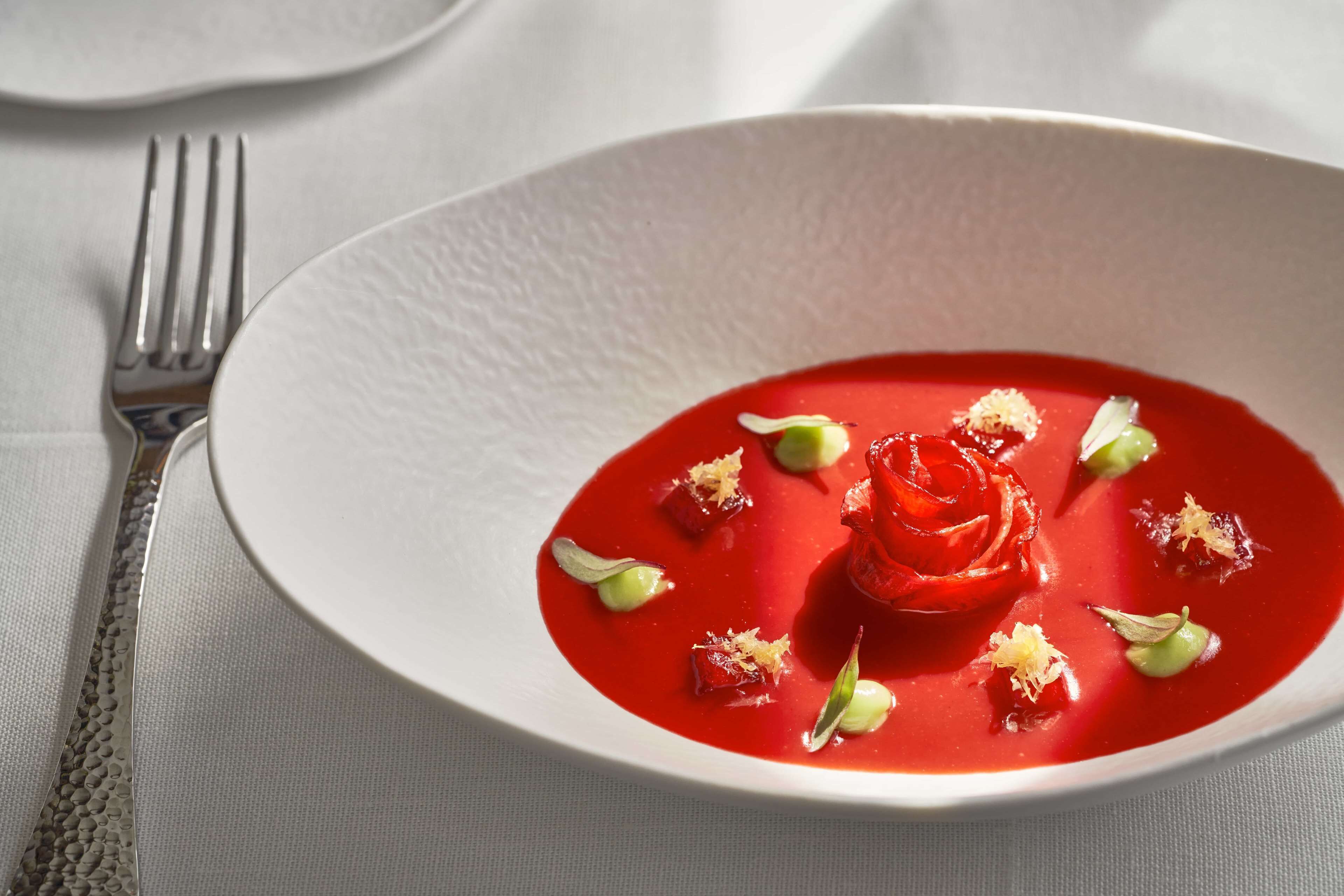 Plato blanco con sopa roja adornada con hierbas verdes y una rosa.