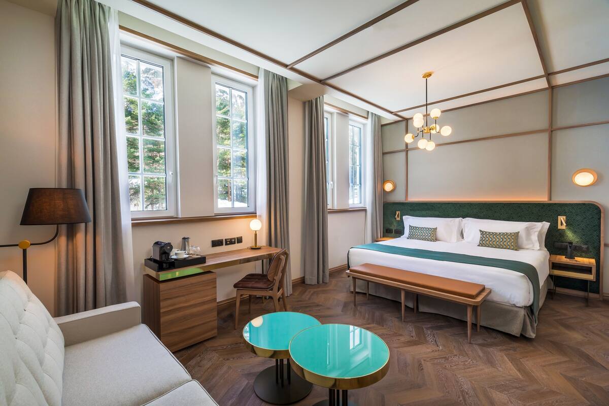 A hotel room with a bed, desk, chair, two round tables, and a sofa.