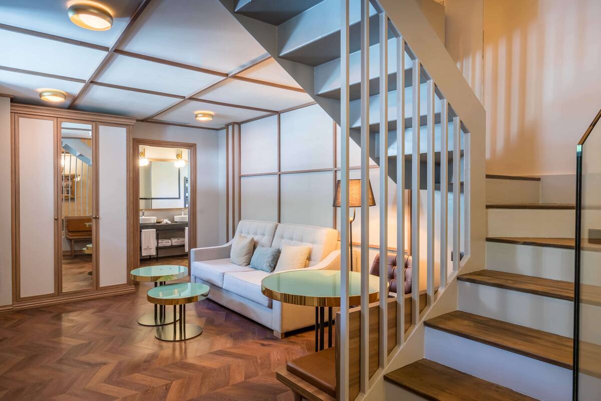A modern interior with a staircase, a white sofa, and a dining area with glass tables.