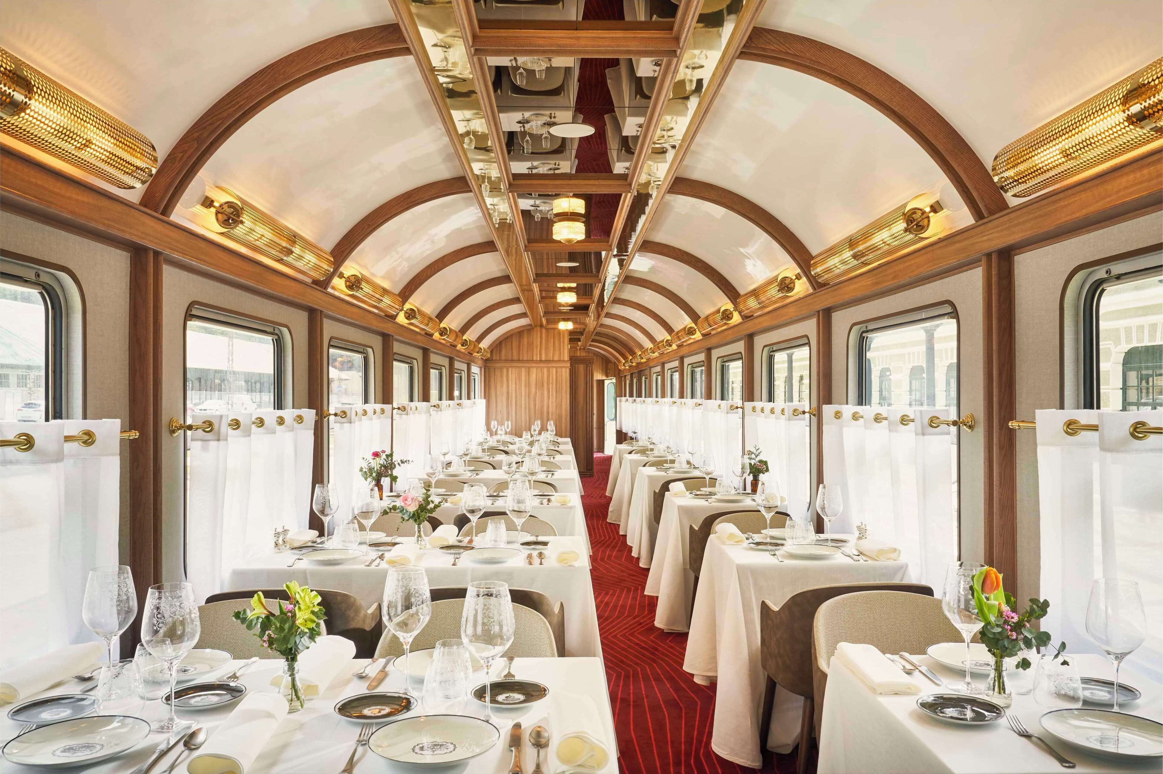 A dining car with tables set for a meal, featuring a red carpet and white tablecloths.