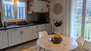 A kitchen with white cabinets, a dining table with a basket, and a view of a green landscape through the window. - Large, comfortable house with exceptional mountain views (Laruns)