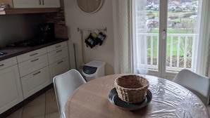 A kitchen with white cabinets, a clock, and a view of a green landscape through a sliding glass door. - Large, comfortable house with exceptional mountain views (Laruns)