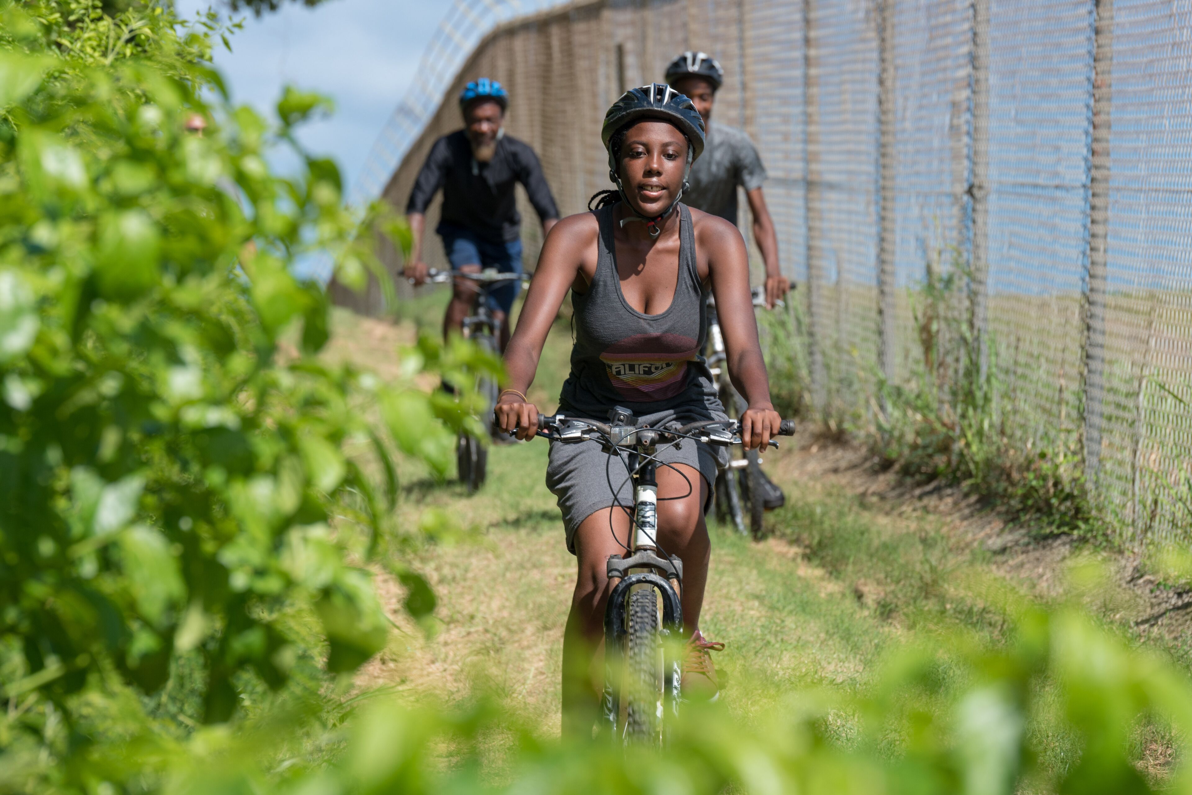 A person riding a bicycle on a path with a fence in the background.