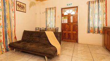 Ein Zimmer mit einer braunen Couch, einer Holztür mit einem Ausgangsschild und gemusterten Vorhängen.