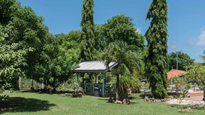 A lush garden with a gazebo, tall trees, and a small building with a metal roof. - Eco Park Inn (Crown Point)