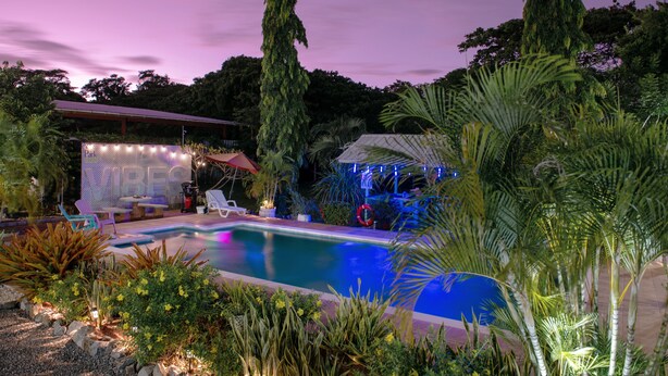 A swimming pool surrounded by tropical plants and a covered area with string lights. - Eco Park Inn (Crown Point)
